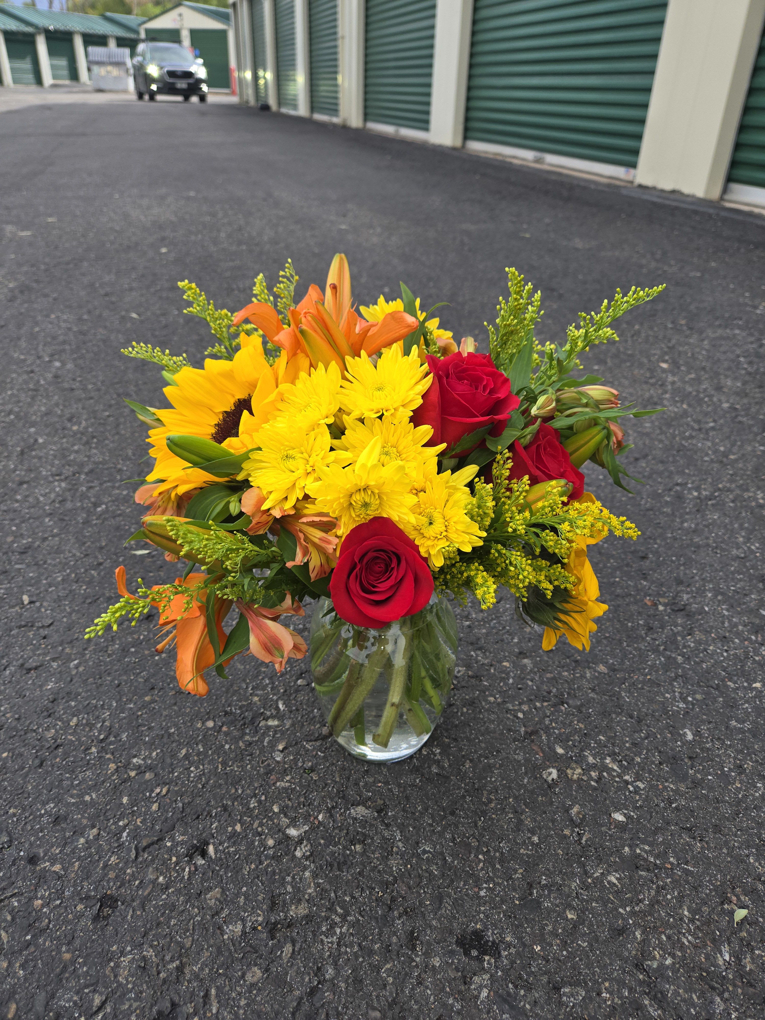Bouquet of red roses, yellow daisies, and orange lilies in a glass vase