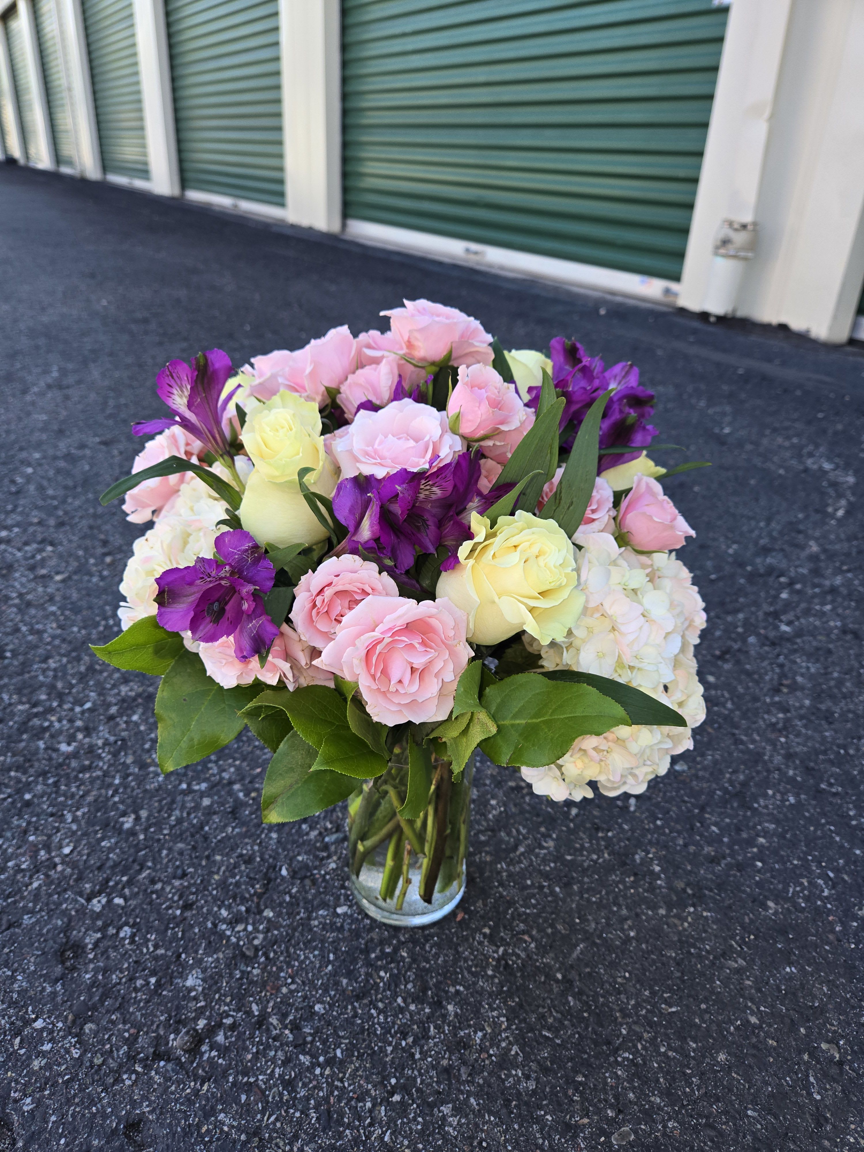 Pink and yellow roses with purple flowers in a glass vase
