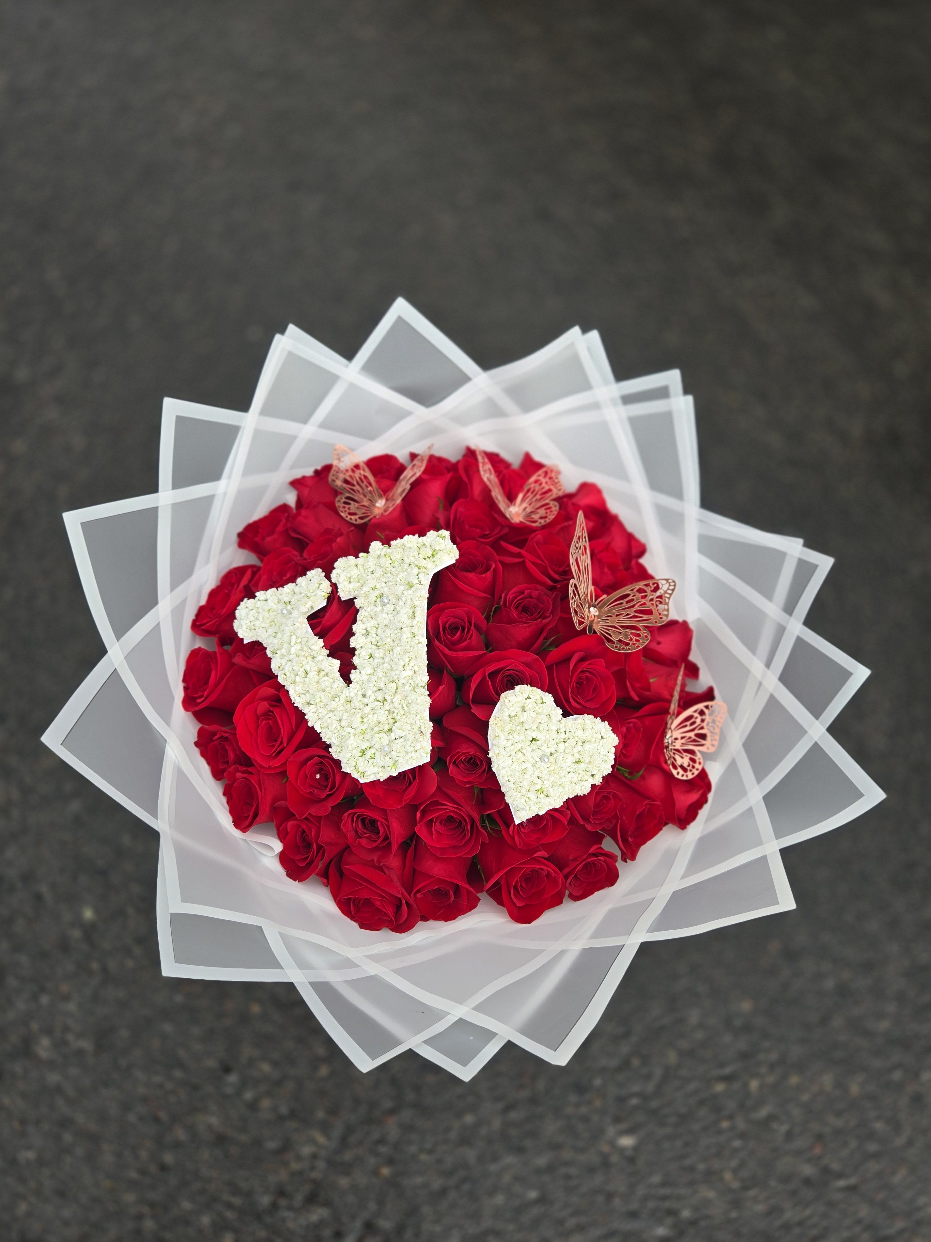 Round bouquet of red roses with white floral letters and butterfly accents