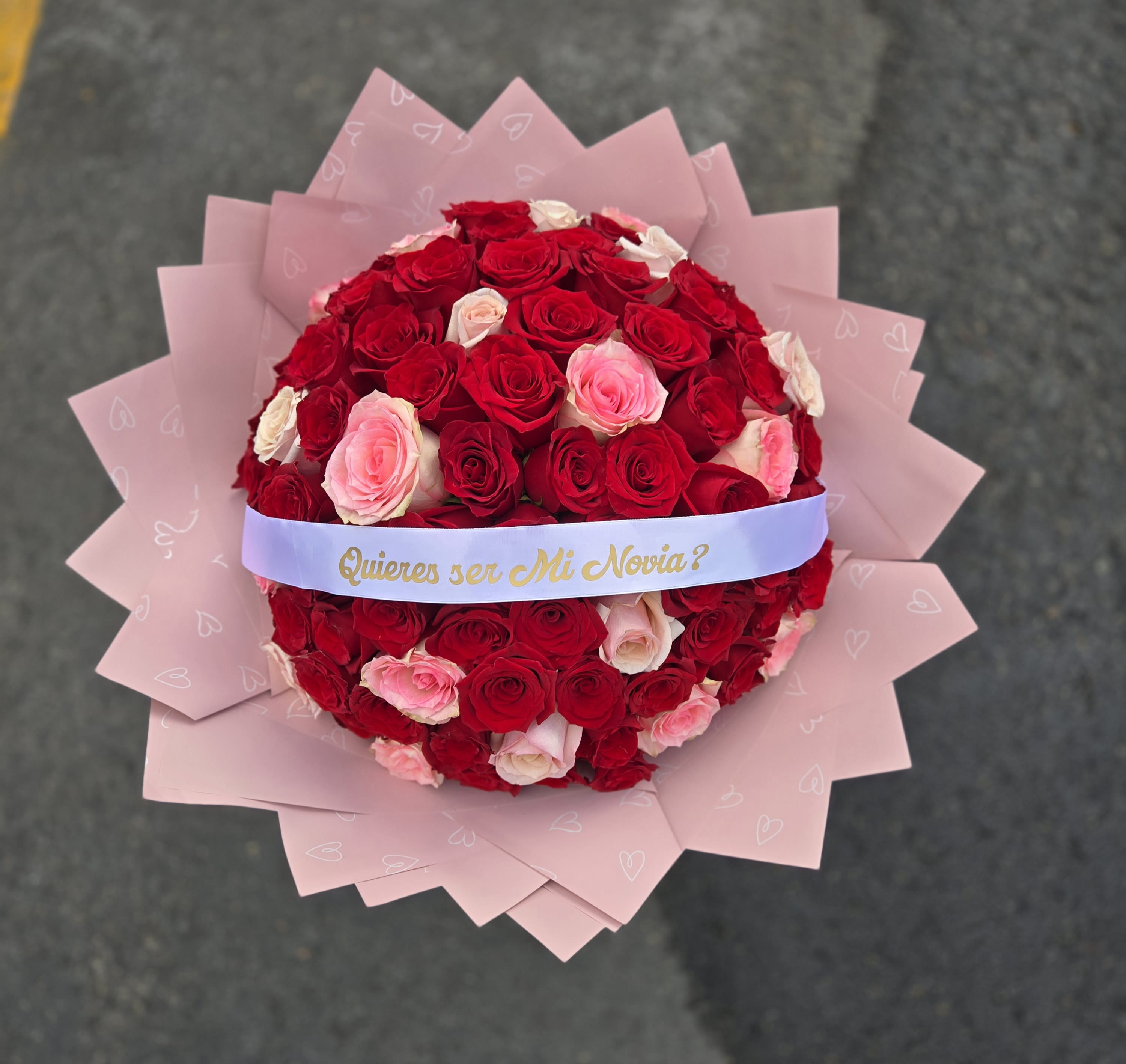 Round bouquet of red and pink roses wrapped in pink paper with a ribbon