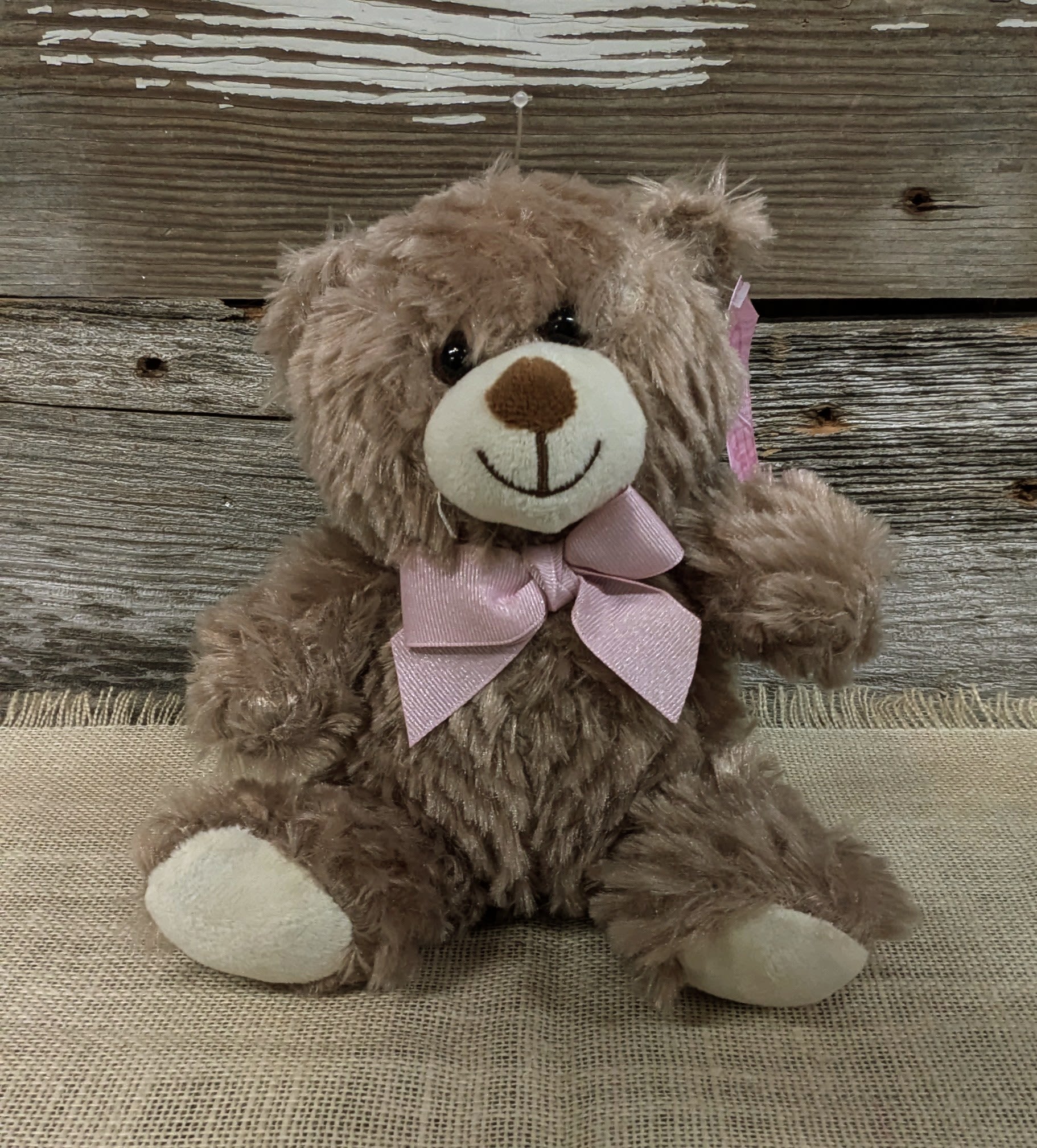 Brown teddy bear with a pink bow sitting on burlap
