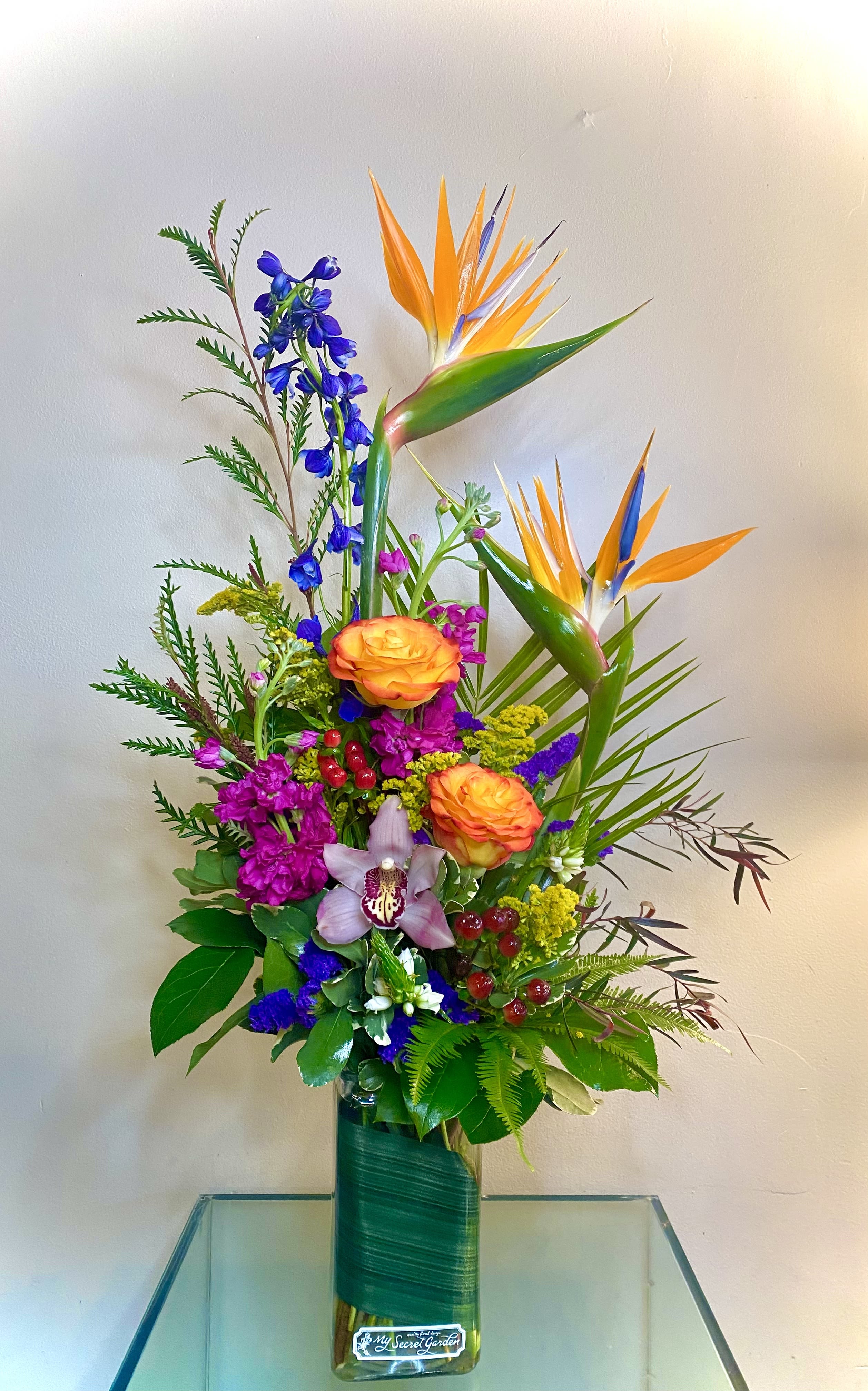 Tropical bouquet with orange bird-of-paradise and mixed blooms in a glass vase