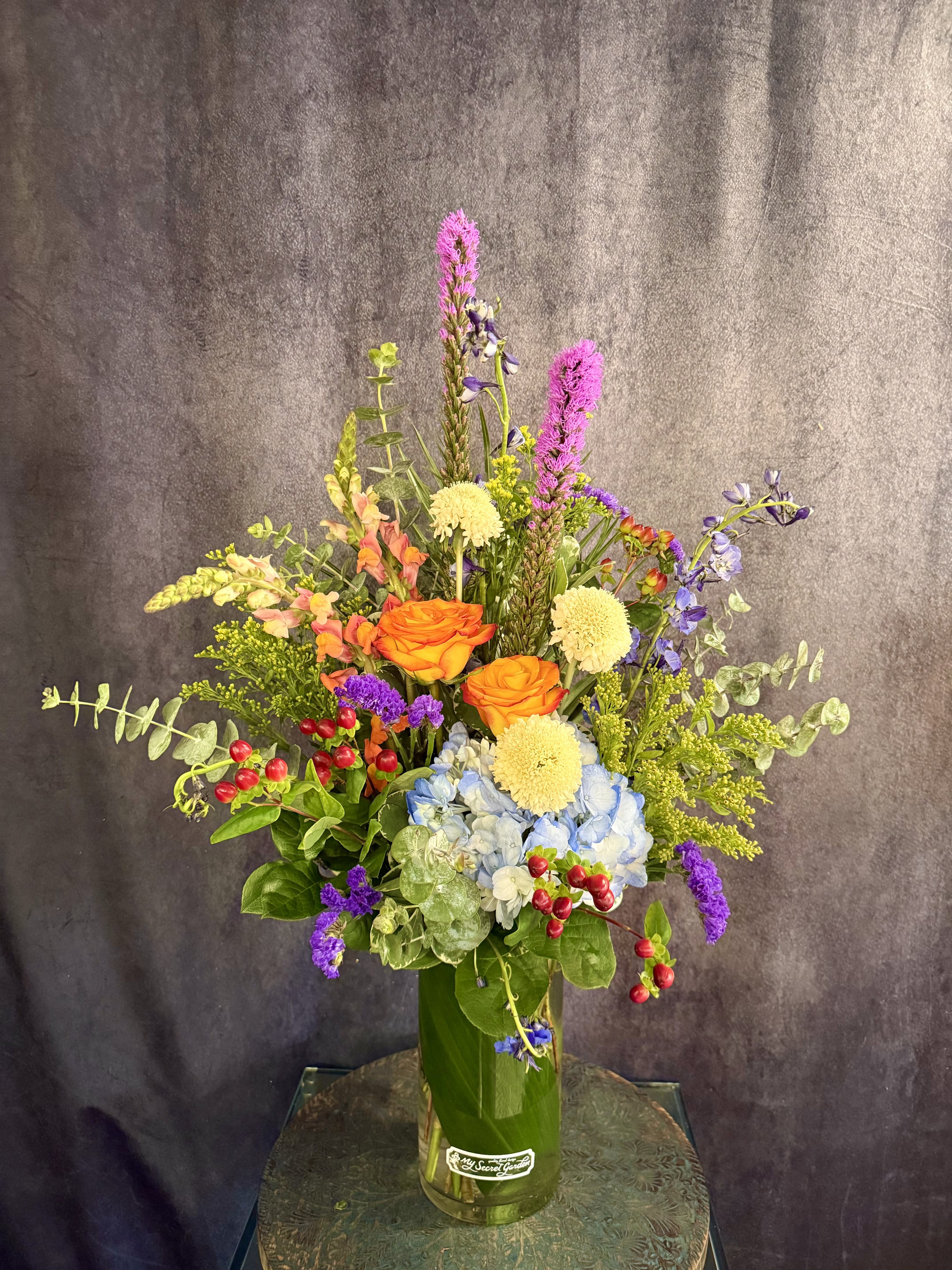 Splash of Summer - This stunning tall modern arrangement filled with vibrant colors such as red, blue, yellow and orange is perfect for the summer. With beautiful bi-color roses, scabiosa, delphinium, and snapdragons, this arrangement is sure to bring a splash of summer to your day!