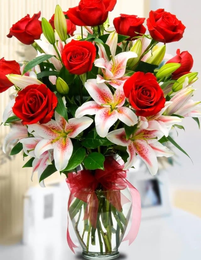 Red roses and white lilies in a clear glass vase with a red ribbon