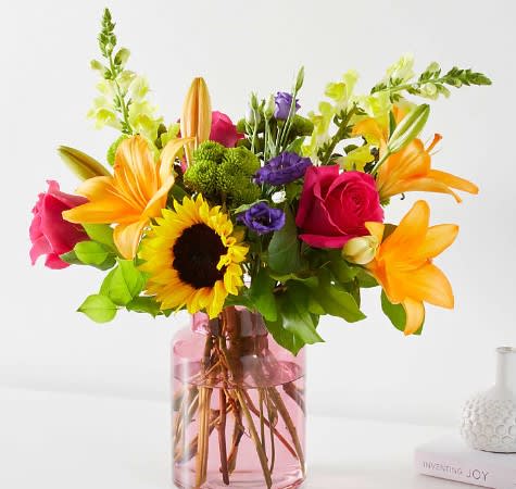 Mixed bouquet with roses, lilies, and a sunflower in a pink glass vase