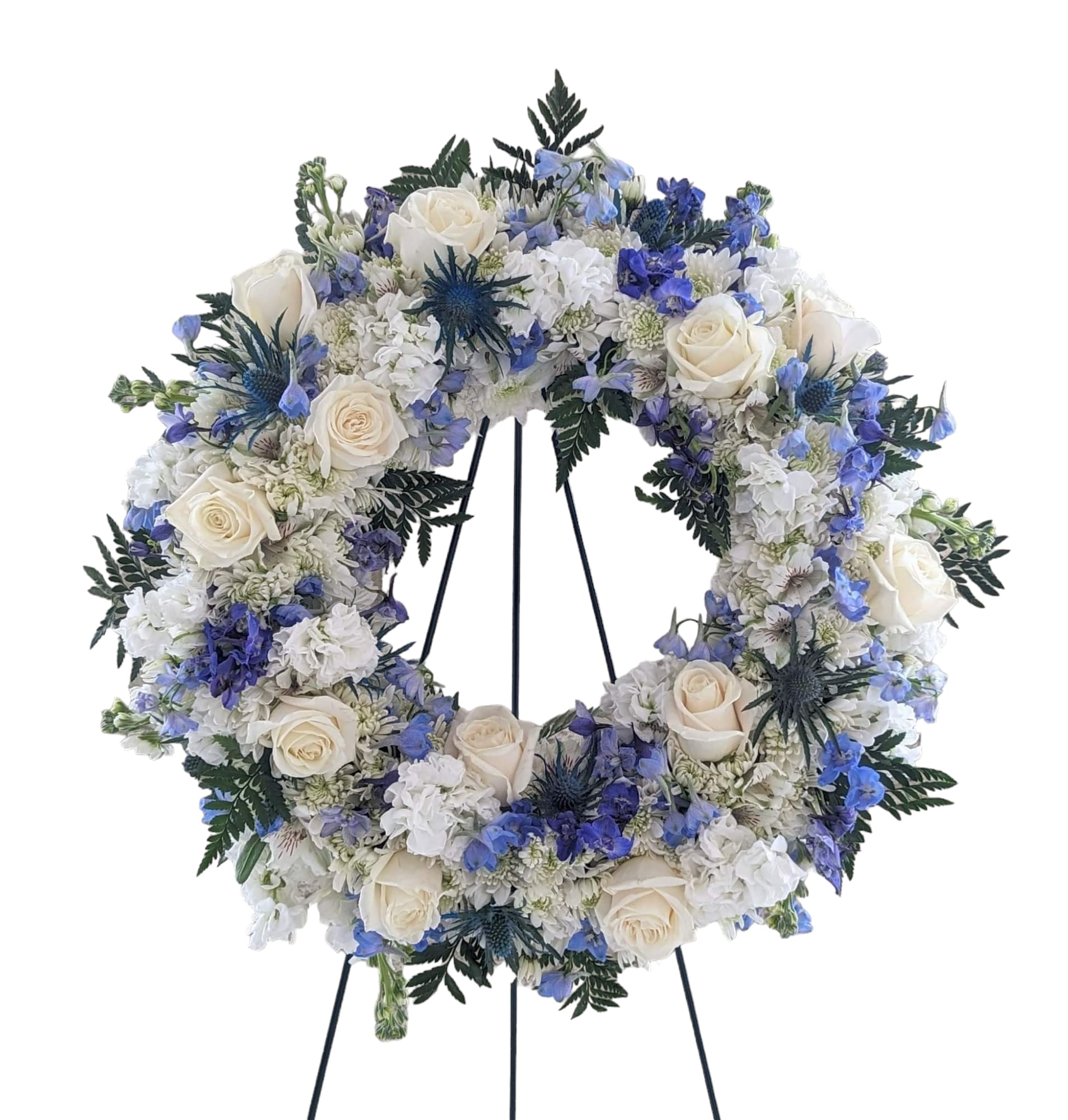 Circular floral wreath with white roses and blue flowers on a stand