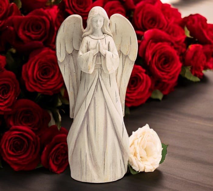 White angel figurine in front of red roses with a cream rose at the base