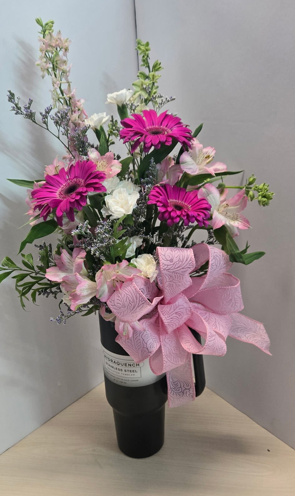 Blossom Brew by Art &amp; Flowers - Introducing "Blossom Brew" – a unique floral arrangement presented in a 40oz tumbler with a handle, combining the beauty of fresh flowers with the charm of your favorite drinkware. Bursting with vibrant blooms, this arrangement is a delightful centerpiece for any occasion. After the blooms have faded, repurpose the tumbler for your favorite hot and cold beverages for a gift that will last. Flowers will be chosen to complement the color of the tumbler, and will be a beautiful and vibrant seasonal mix.   Includes a beautiful and fresh assortment of vibrant seasonal blooms in a 40oz insulated tumbler. Tumbler colors vary, including: Black, white, purple, blue and more.