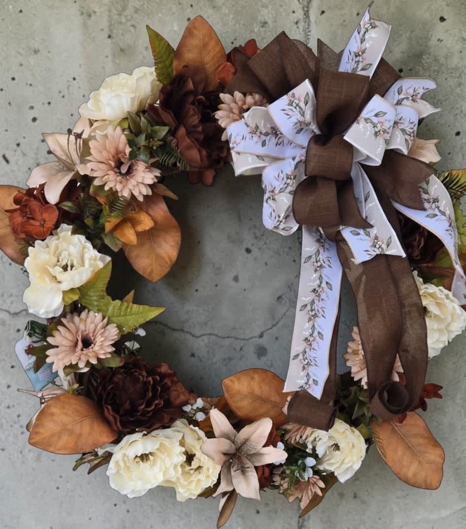 Floral wreath with cream blooms, brown flowers, and a large ribbon bow