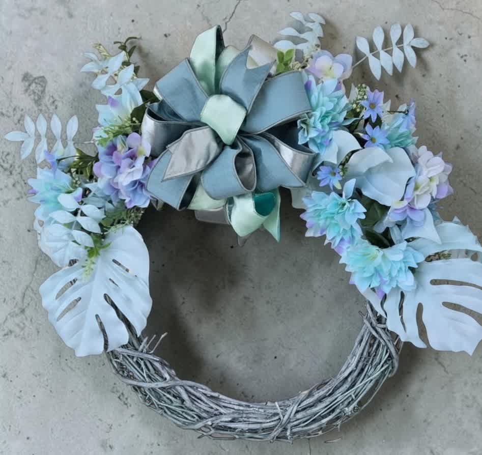 Pastel floral wreath with a large ribbon bow and white monstera leaves