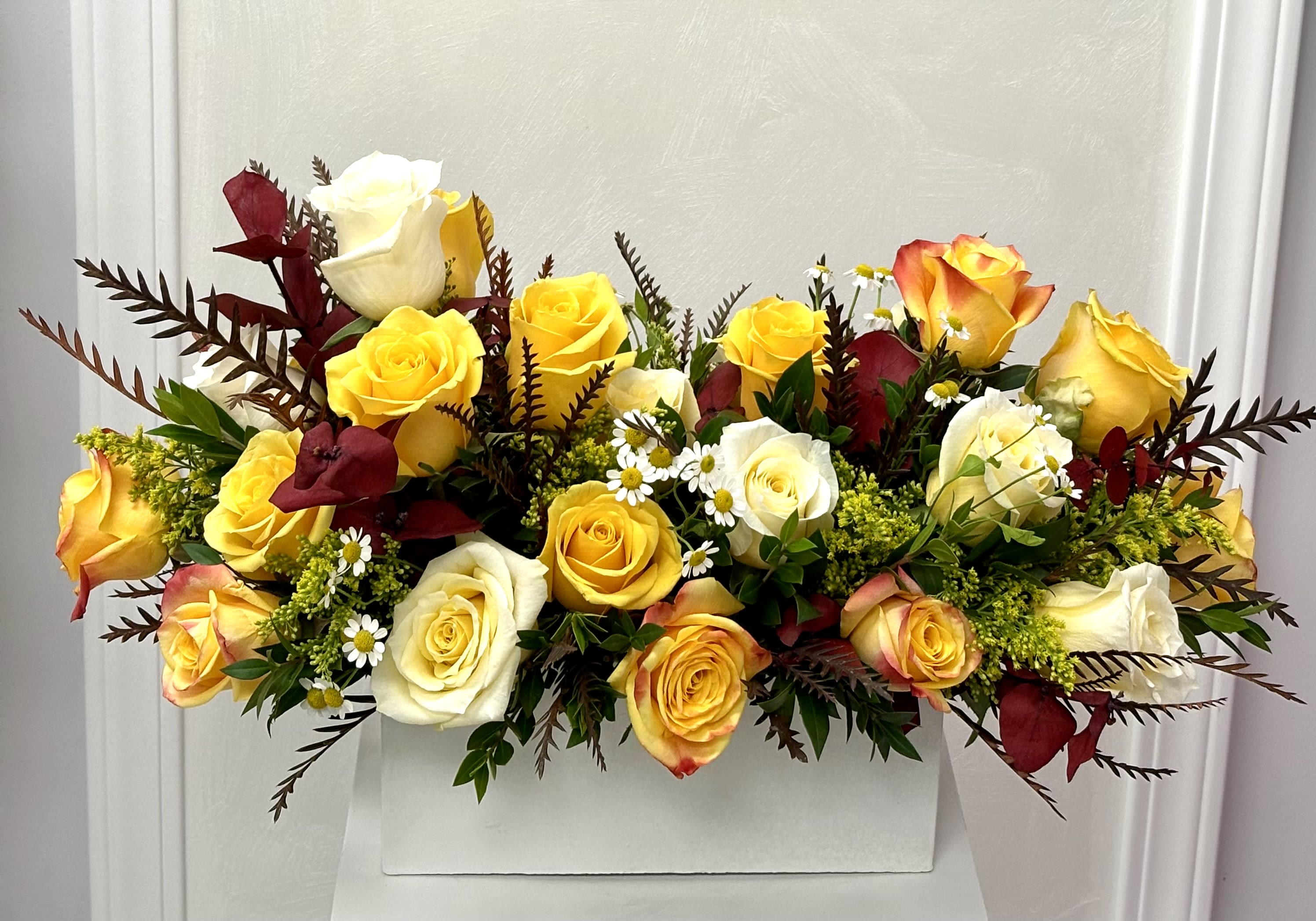 Yellow and white roses arranged in a white box with burgundy accents