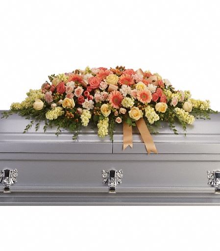T266-3A Warmest Remembrance Casket Spray - This tastefully colorful casket spray is not only a tribute to a lost loved one, but a reminder of the many joyous times spent together. The beautiful bouquet includes peach roses, light pink spray roses, coral spray roses, light orange gerberas, light orange carnations, light yellow stock and peach hypericum, accented with satin ribbon and assorted greenery. Approximately 50" W x 17 1/2" H 
