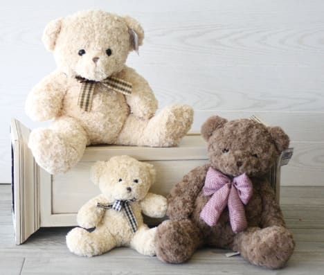 Three teddy bears with ribbon bows arranged on a wooden crate