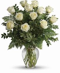 White roses in a clear glass vase with greenery
