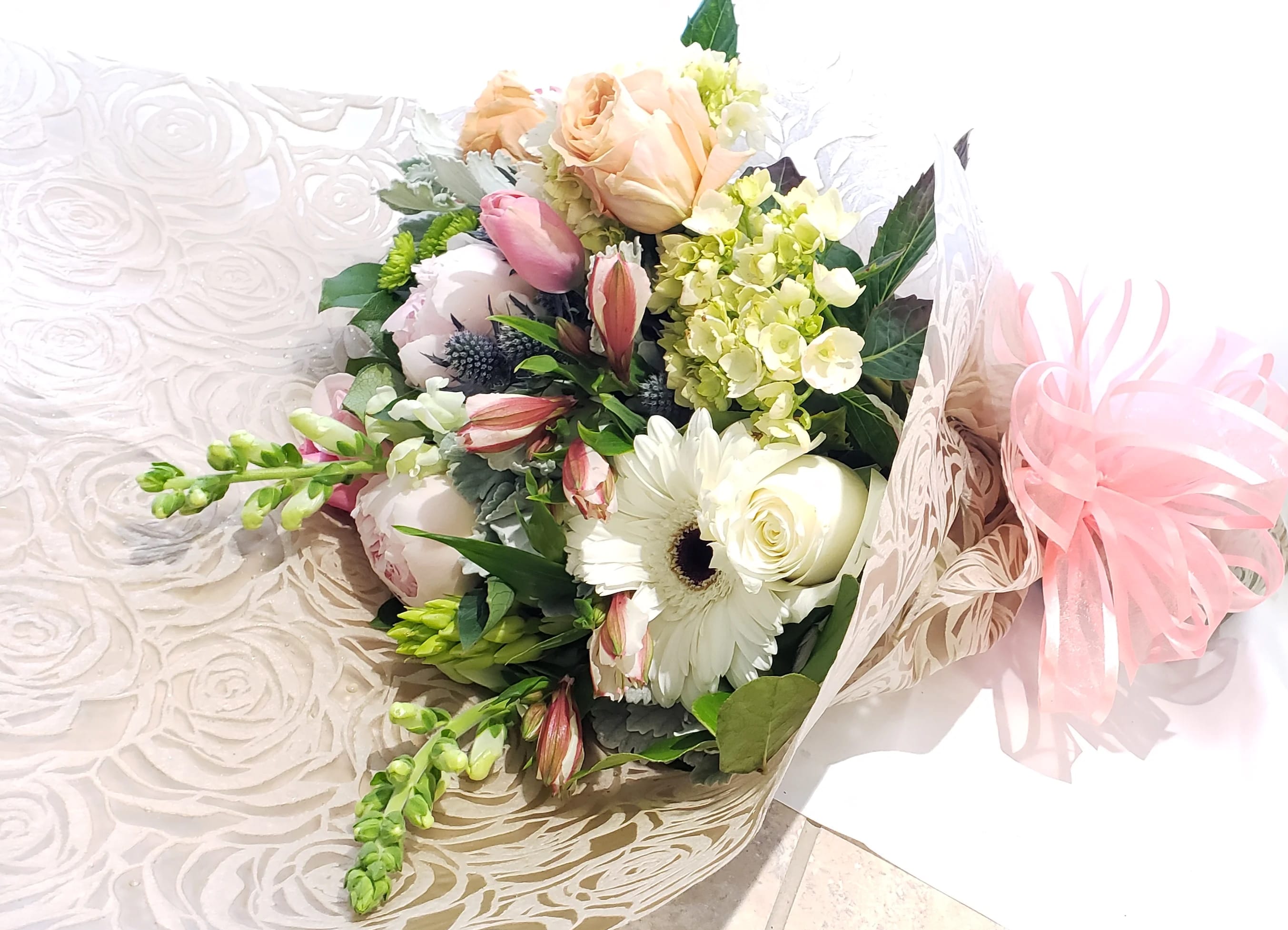 Bouquet of white and blush flowers wrapped in patterned paper with a pink ribbon