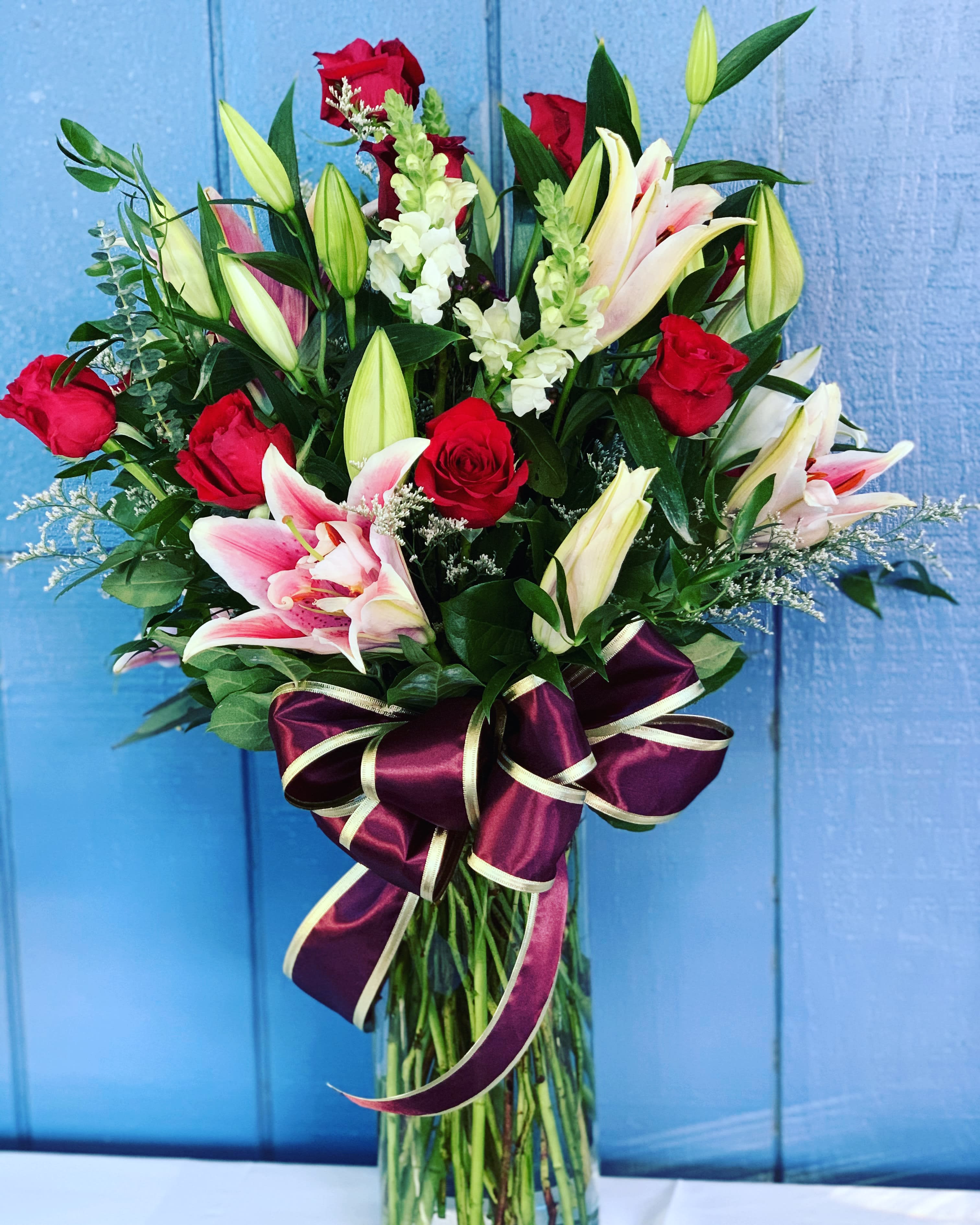 Bouquet of red roses and pink lilies in a clear glass vase with a purple ribbon
