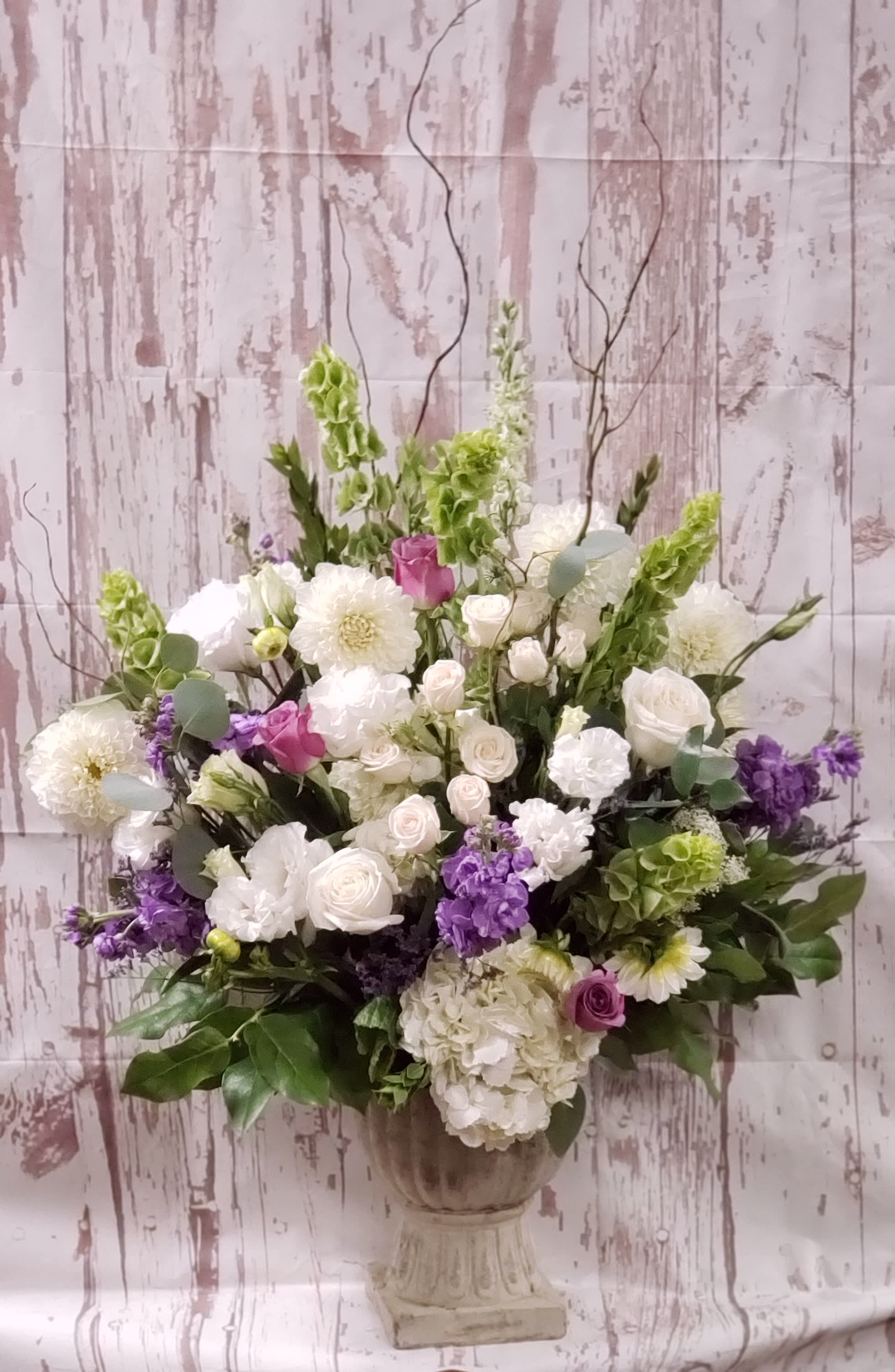 Large mixed floral arrangement in a pedestal vase with white, purple, and green blooms