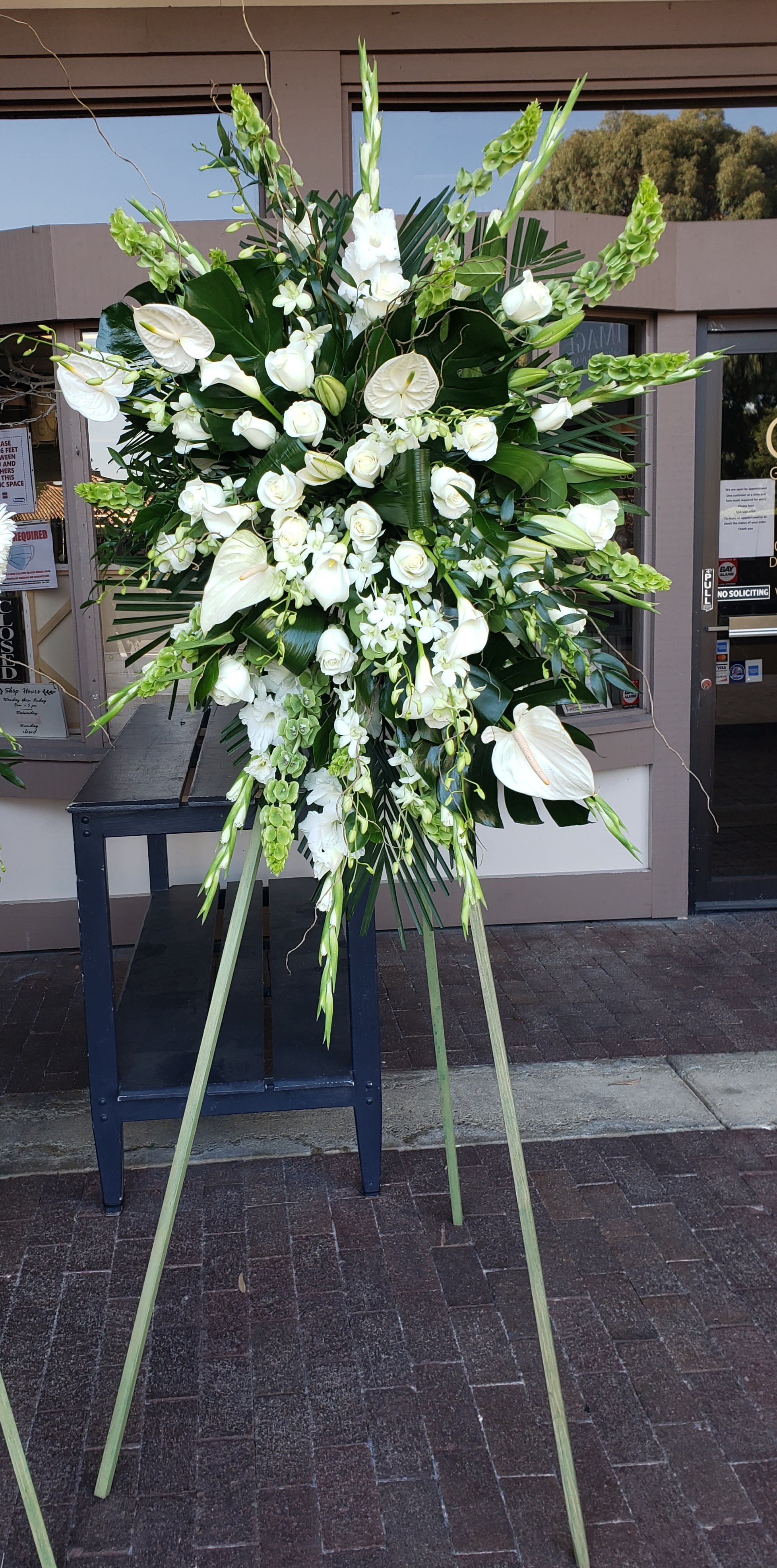Large white funeral spray on a stand with lilies, roses, and orchids