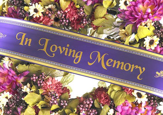 Purple memorial ribbon over a floral wreath with pink, yellow, and white flowers