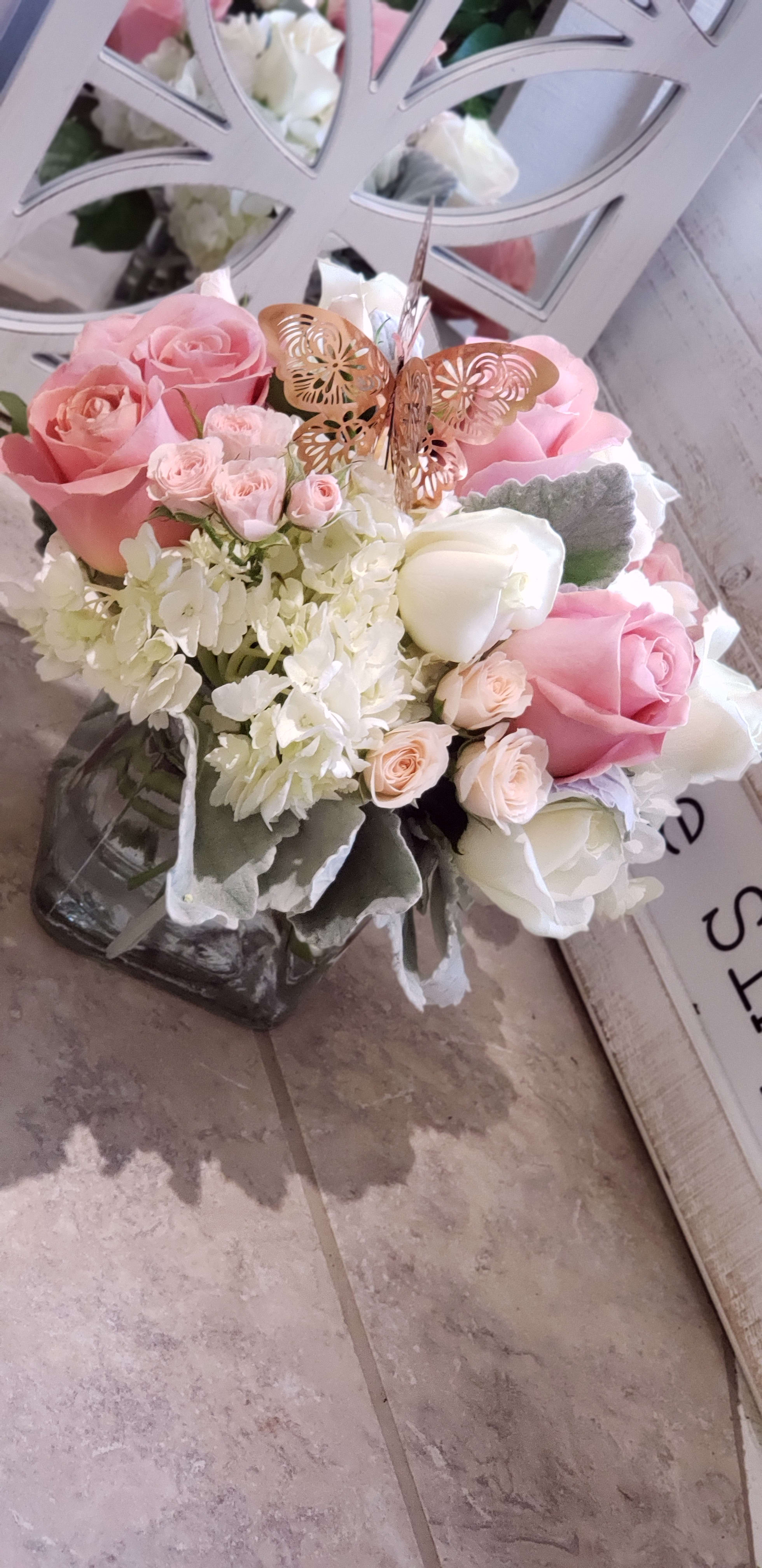 Pink and white rose bouquet in a glass vase with a butterfly pick