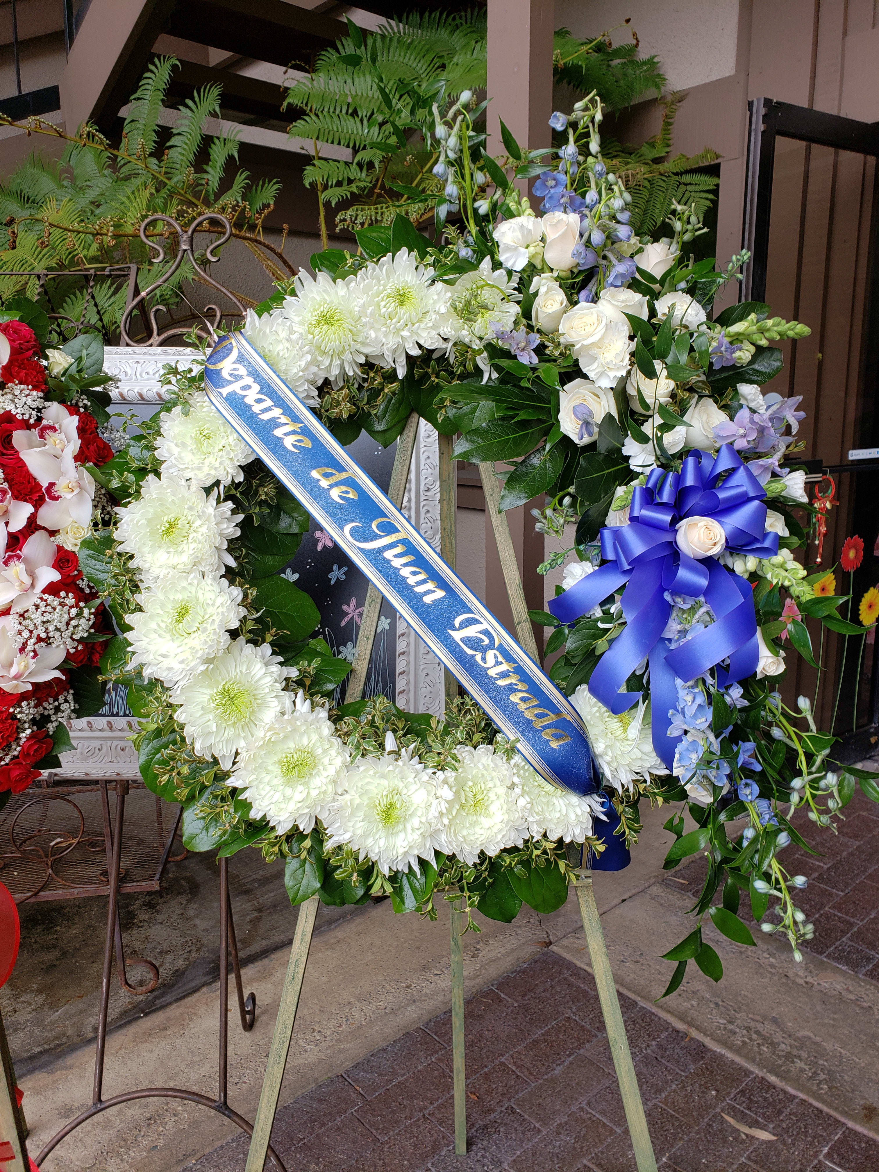 Large funeral wreath with white flowers and a blue memorial ribbon