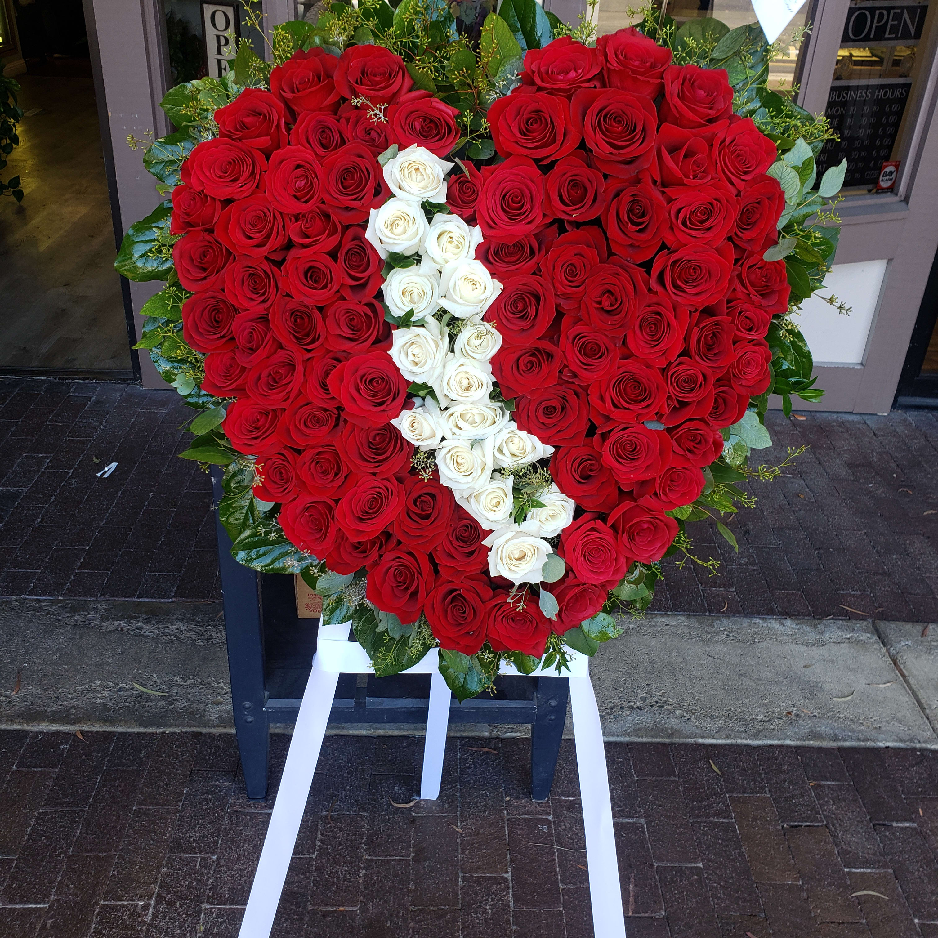Heart-shaped red and white rose arrangement on an easel with white ribbon