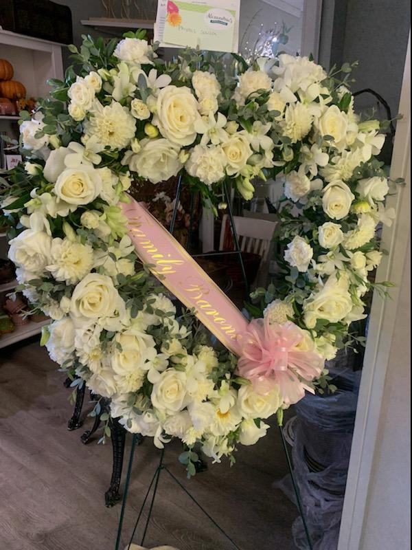 Heart-shaped white floral wreath with a pink ribbon and bow