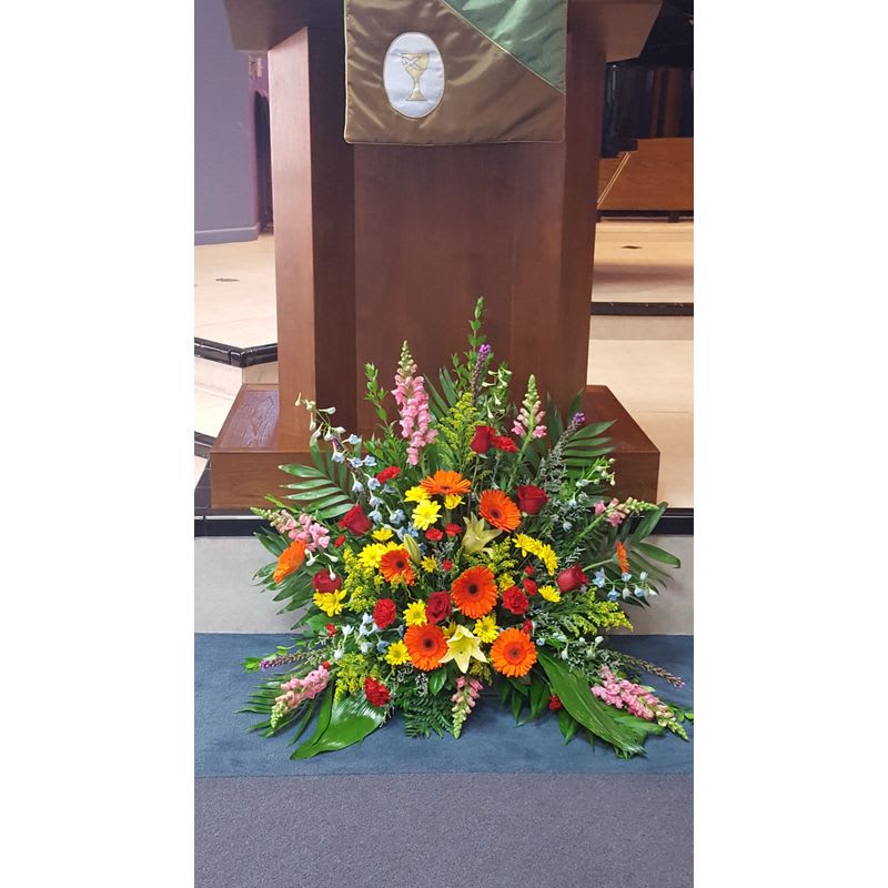 Large mixed floral arrangement at a podium with bright orange, yellow, red, and pink blooms
