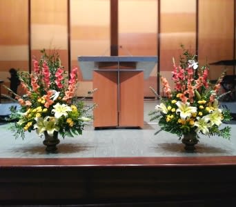Two large floral arrangements flank a podium on a stage.