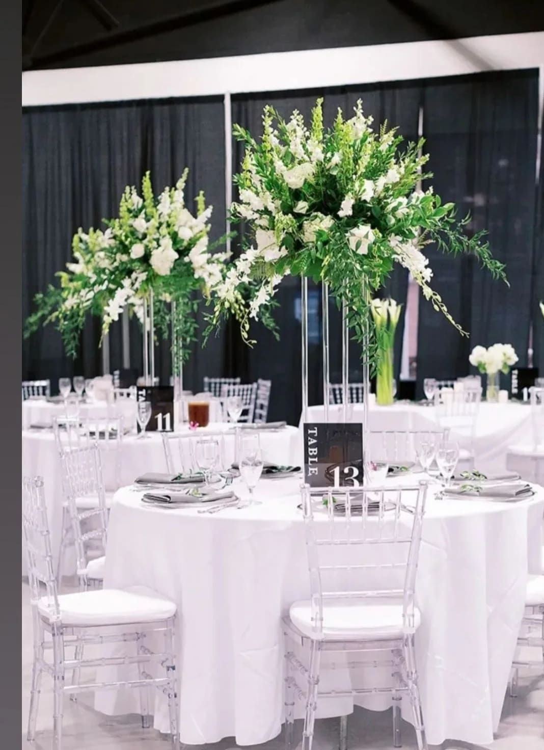 Tall white floral centerpieces on clear stands at round banquet tables