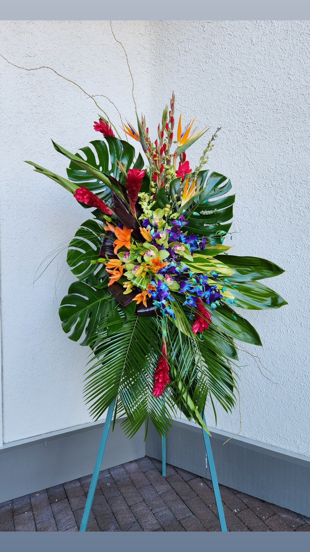 Tall tropical floral spray with bright orchids and red blooms on an easel