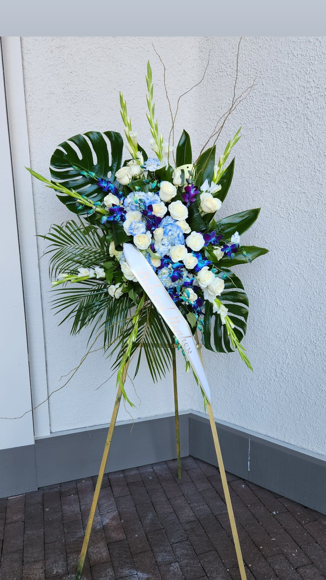 Tall standing floral spray with white roses, blue hydrangeas, and purple orchids