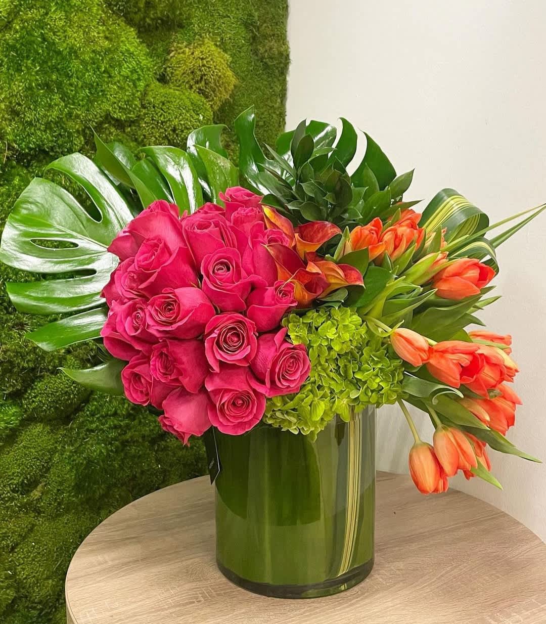 Pink roses and orange tulips arranged in a green glass vase