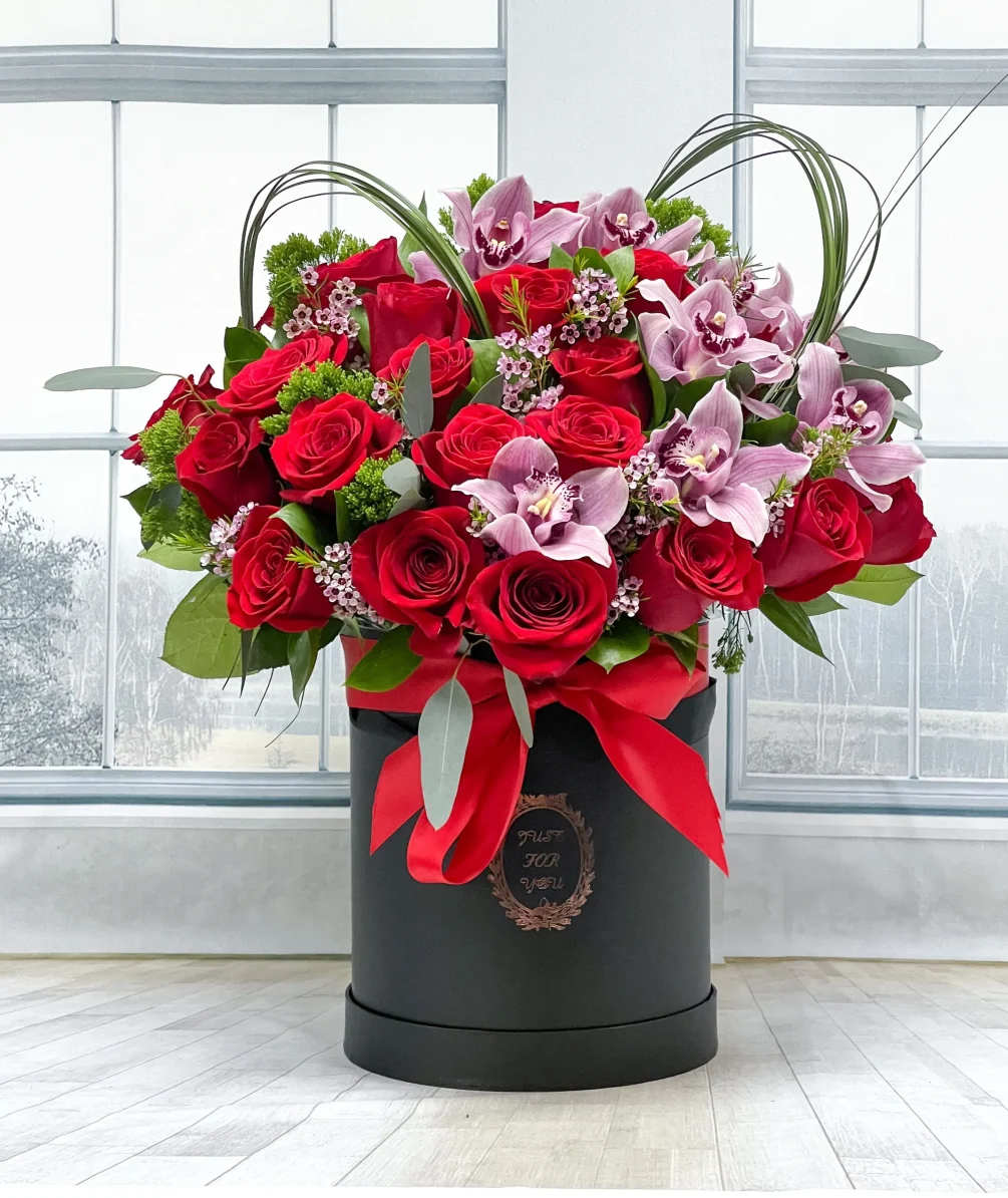 Red roses and pink orchids in a black hatbox with a red ribbon
