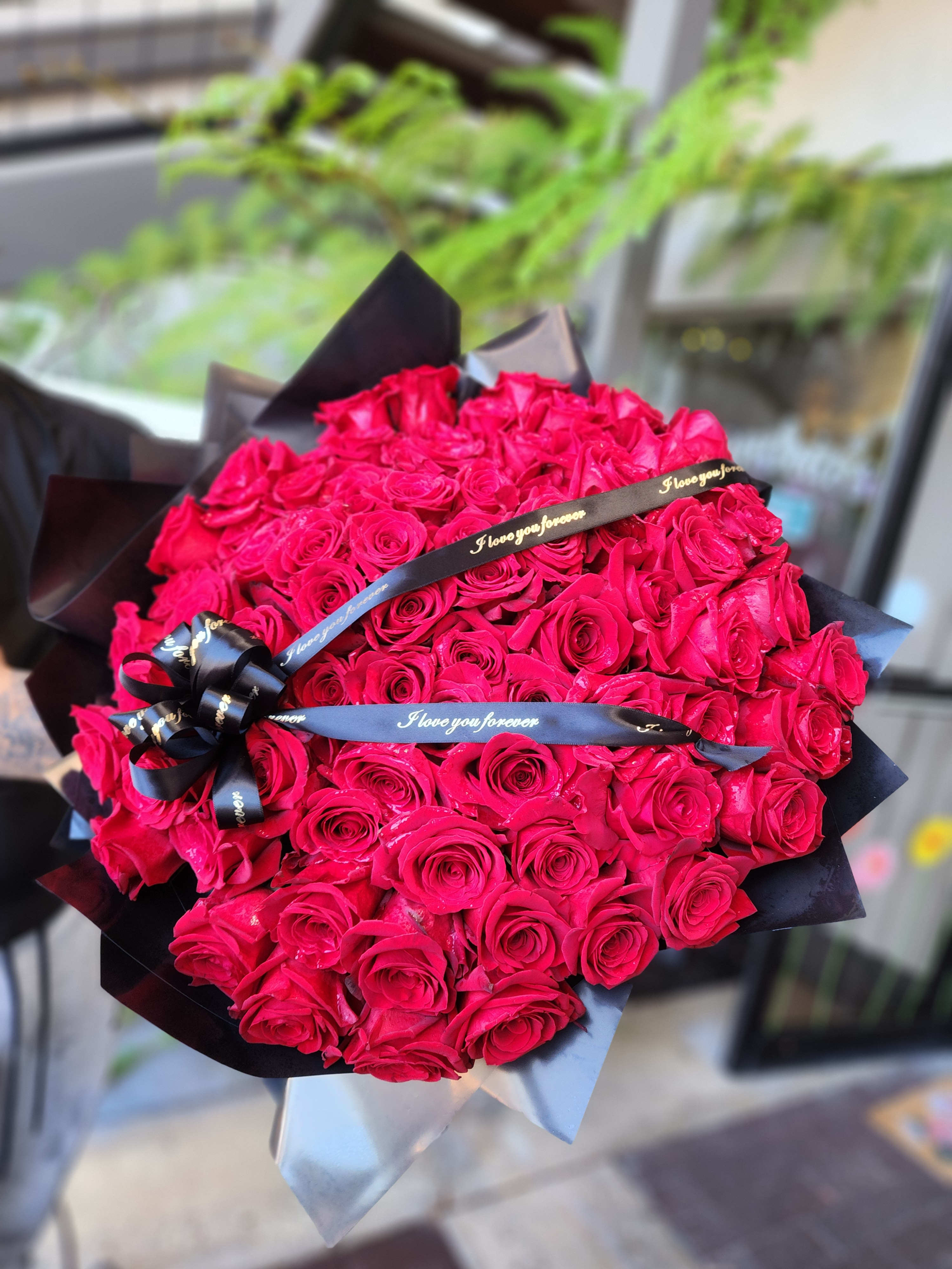 Large bouquet of hot pink roses wrapped in black paper with ribbon