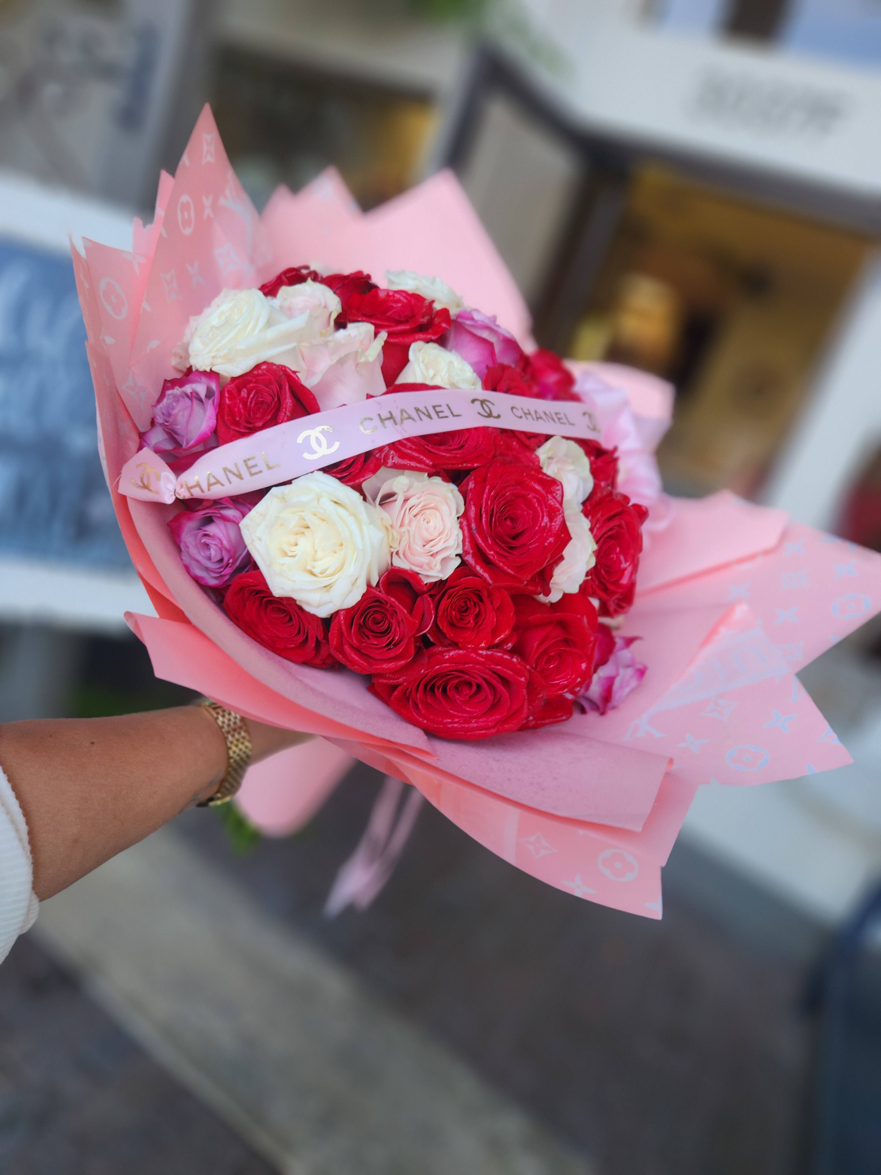 Handheld bouquet of red, white, and pink roses wrapped in pink paper