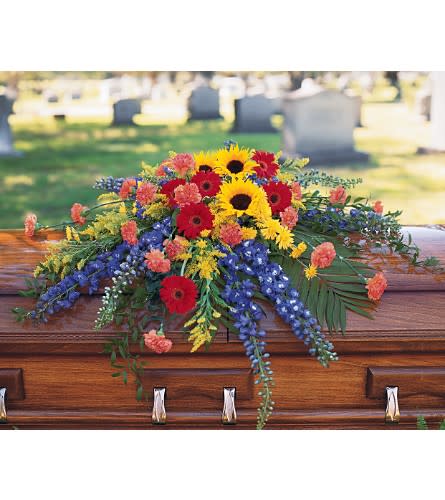 Colorful floral spray on a casket with sunflowers and red daisies