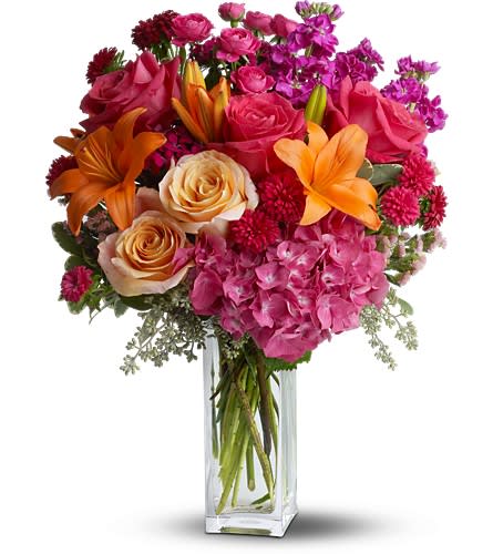 Mixed bouquet of pink roses, orange lilies, and hydrangeas in a glass vase