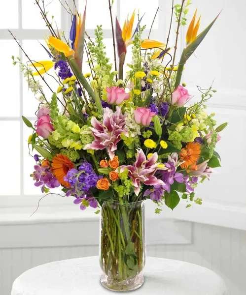Tall mixed bouquet in a clear glass vase with pink, purple, orange, and yellow flowers