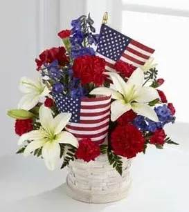 Red, white, and blue floral arrangement in a white basket with American flags