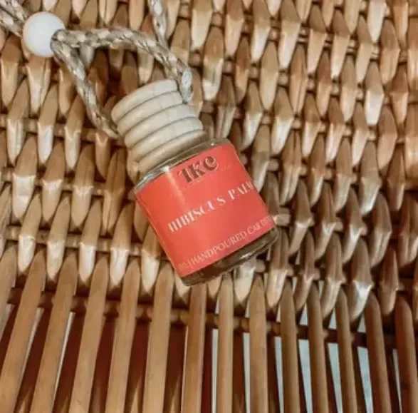 Small perfume bottle with a coral label hanging on a woven surface