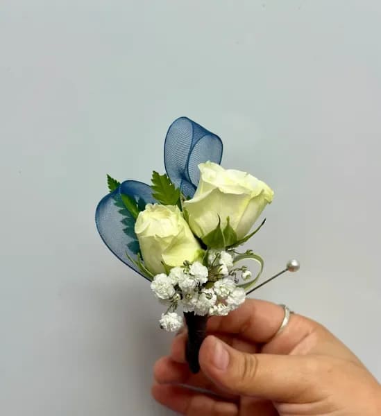 White rose boutonniere with blue ribbon loops and baby's breath