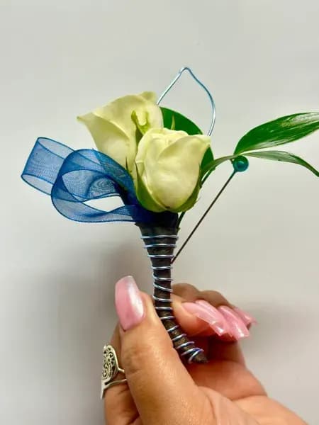 White calla lily boutonniere with blue ribbon and green leaves