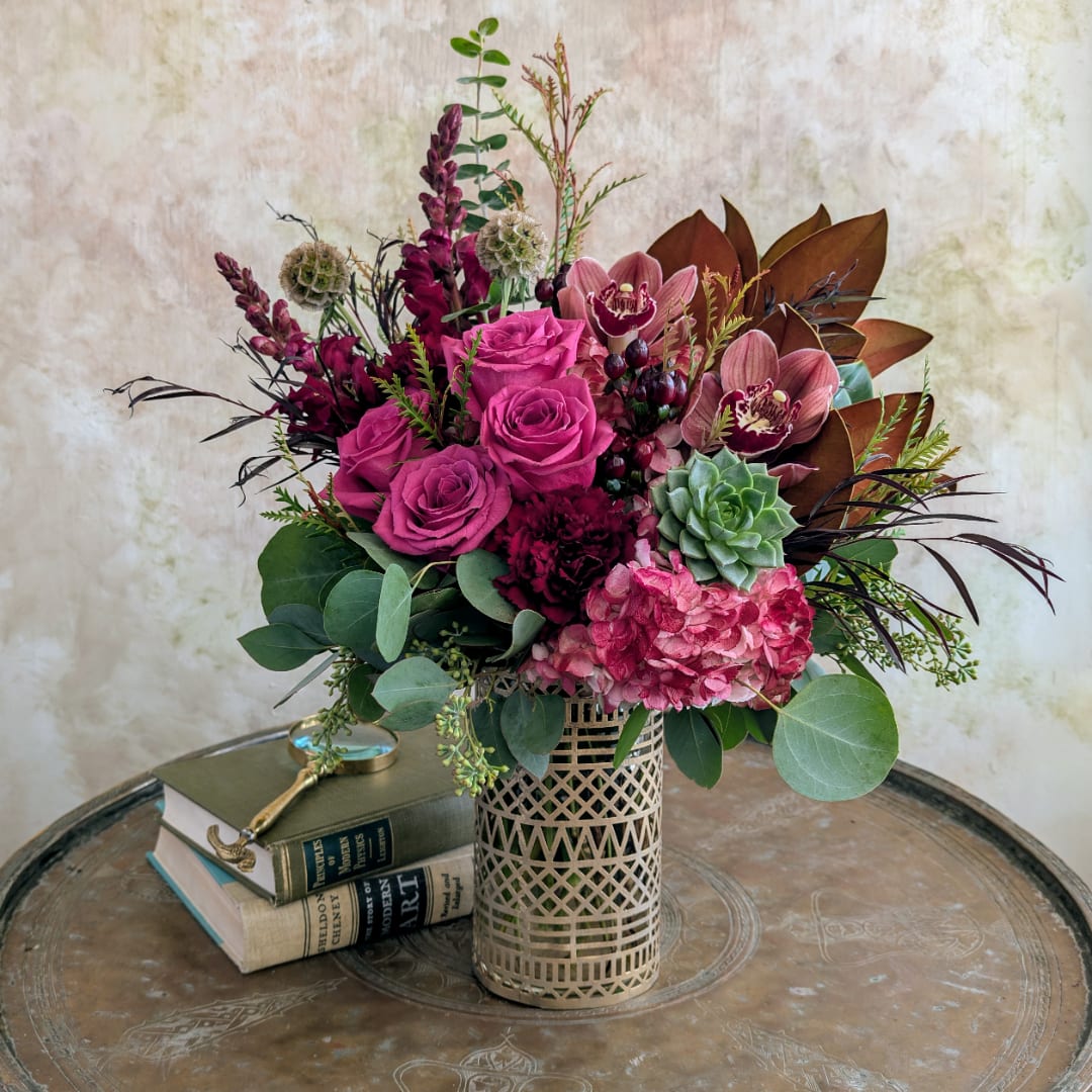 Pink roses and orchids in a patterned gold vase with succulents
