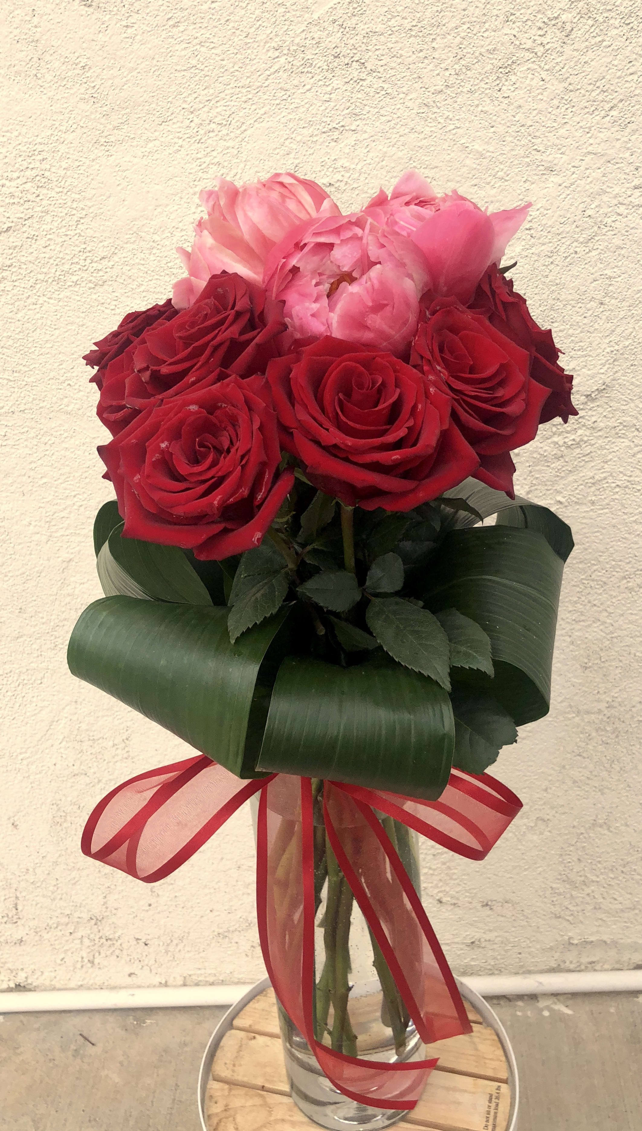 Red and pink roses arranged in a clear glass vase with a red ribbon
