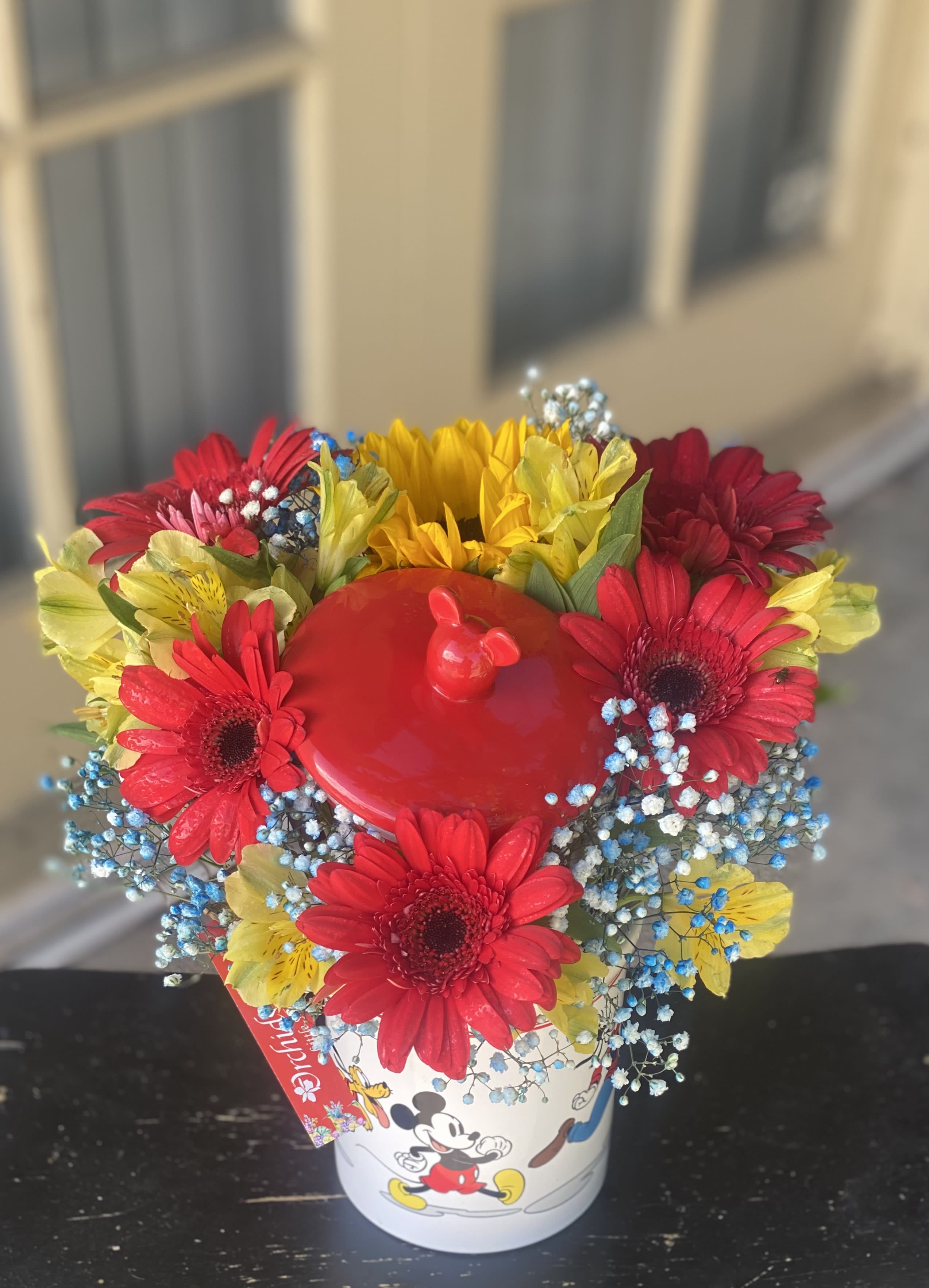 Bright mixed bouquet in a Mickey Mouse bucket with red, yellow, and blue flowers