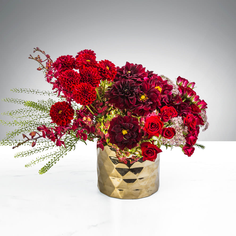 Red and burgundy flower arrangement in a gold vase