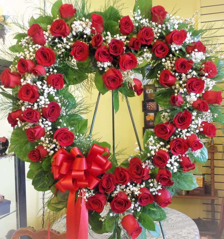 Heart-shaped wreath of red roses with a red bow on a stand
