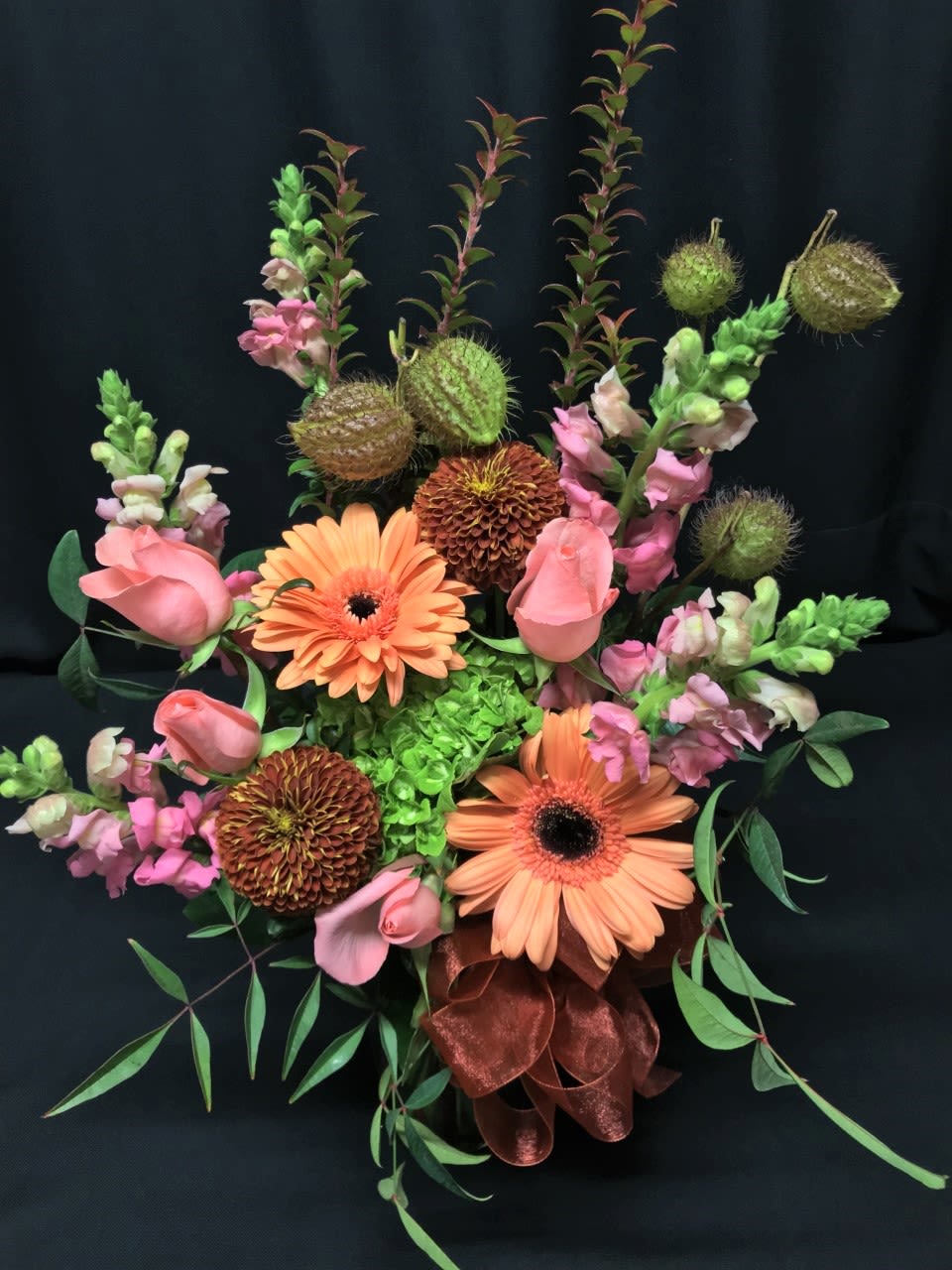 Asclepias Pod Cheerful Mix - Flirty foliage and seed pods accents this autumn design you can use for any special fall event. The green hydrangea blossom sets off the deep rusty cremon and the bright coral roses.* Assortment may vary! Order early for best selection of flowers. 