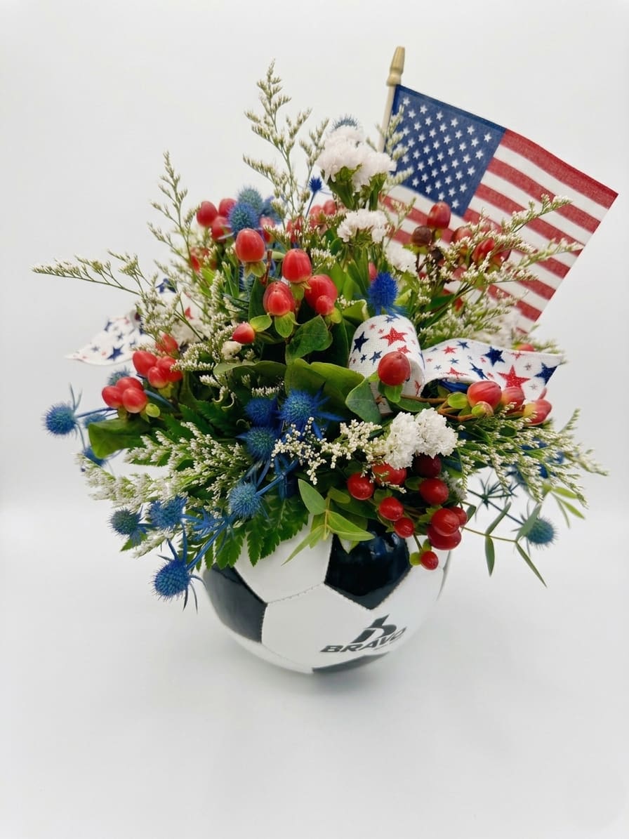 Red, White &amp; Score! - Score major points with this vibrant, patriotic arrangement! Perfect for the sports enthusiast, this unique design features a striking mix of deep blue thistle, bright red hypericum berries, and delicate white fillers, all beautifully arranged inside a classic soccer ball container. Accented with a festive star-patterned ribbon and a mini American flag, it’s a winning choice for celebrations, team victories, or simply showing off some spirited style.